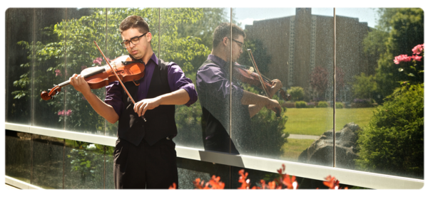 Music major plays violin outside - flowers in the foreground, surface reflecting the university church in the background